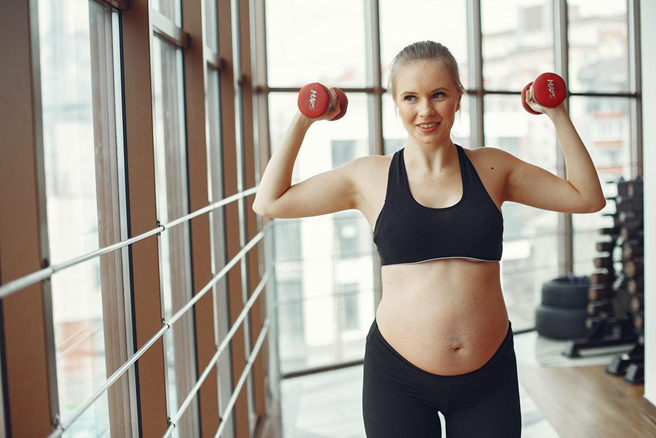 A pregnant woman lifting weights in the gym.